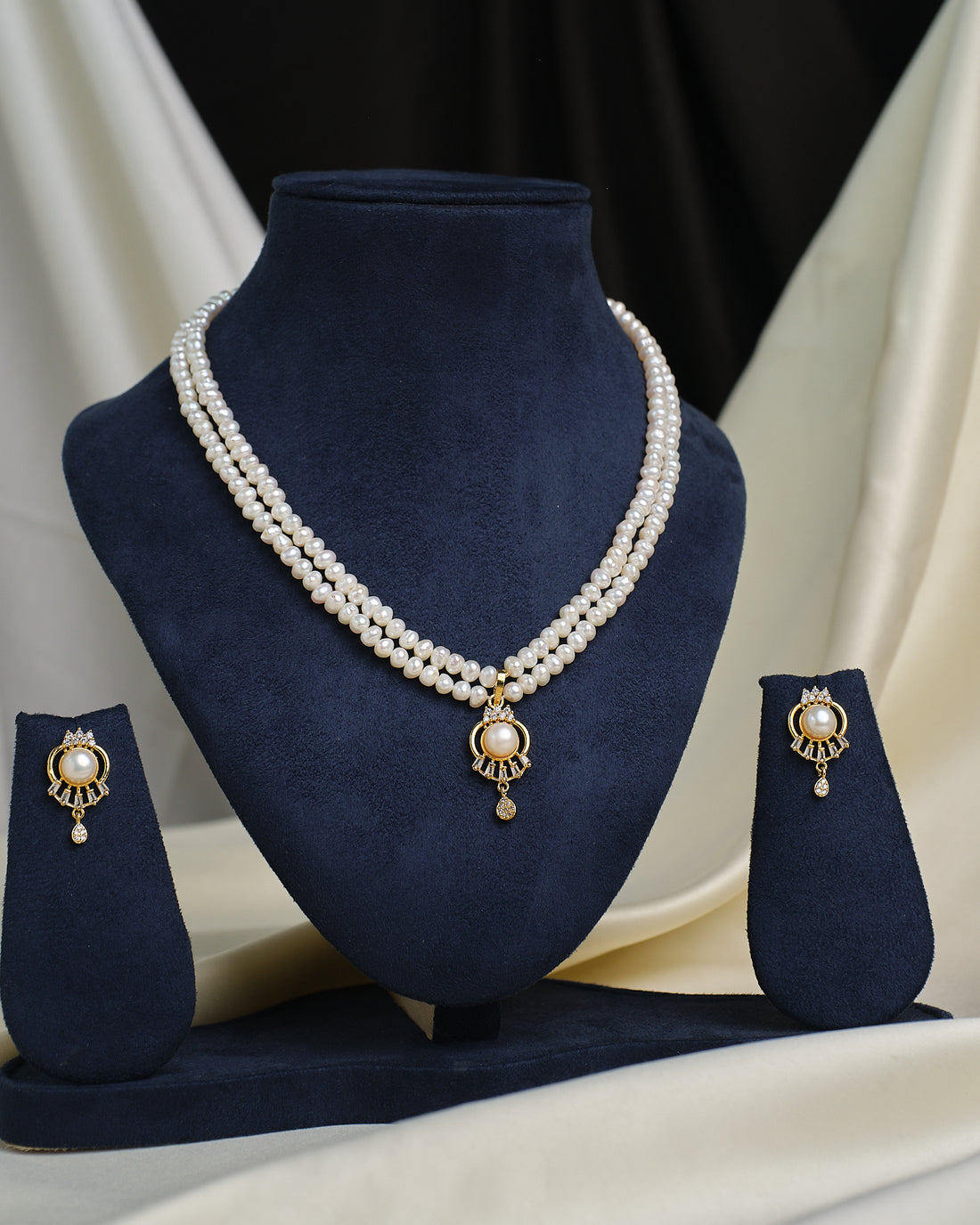 The Chandrani Pearls Sparkling Halo CZ necklace is displayed on a navy blue stand, paired with matching stud earrings on either side, all radiating a luxurious shine.