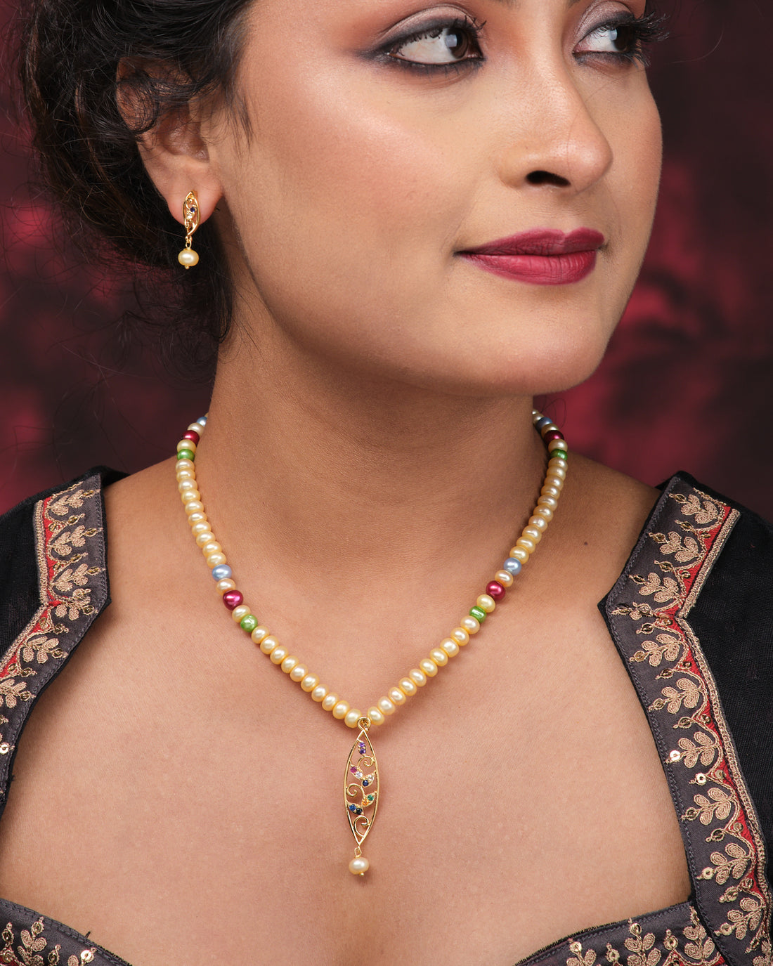 Add a pop of color with Chandrani Pearls’ Colorful One-Line Pearl Set with Earrings, featuring vibrant pearls and matching earrings, beautifully displayed on a pink surface beside elegant purple fabric.