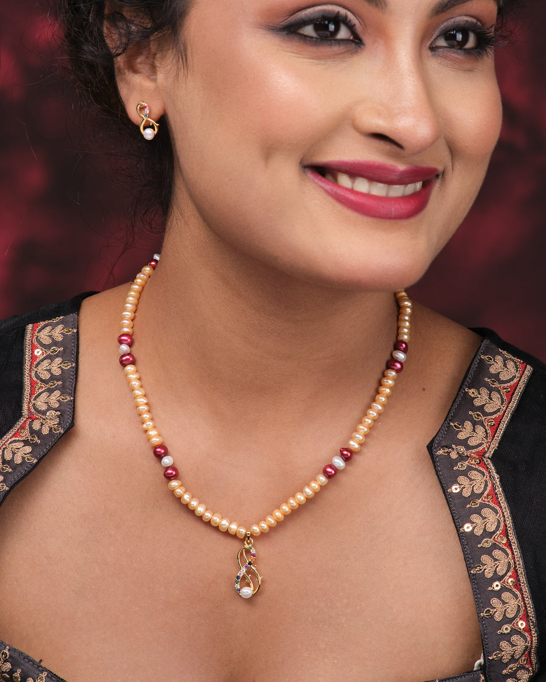 The Elegant Pearl Necklace Set by Chandrani Pearls features a pearl and gold bead necklace with a matching pendant and earrings, displayed on pink with a folded purple cloth, offering subtle design for maximum shine.