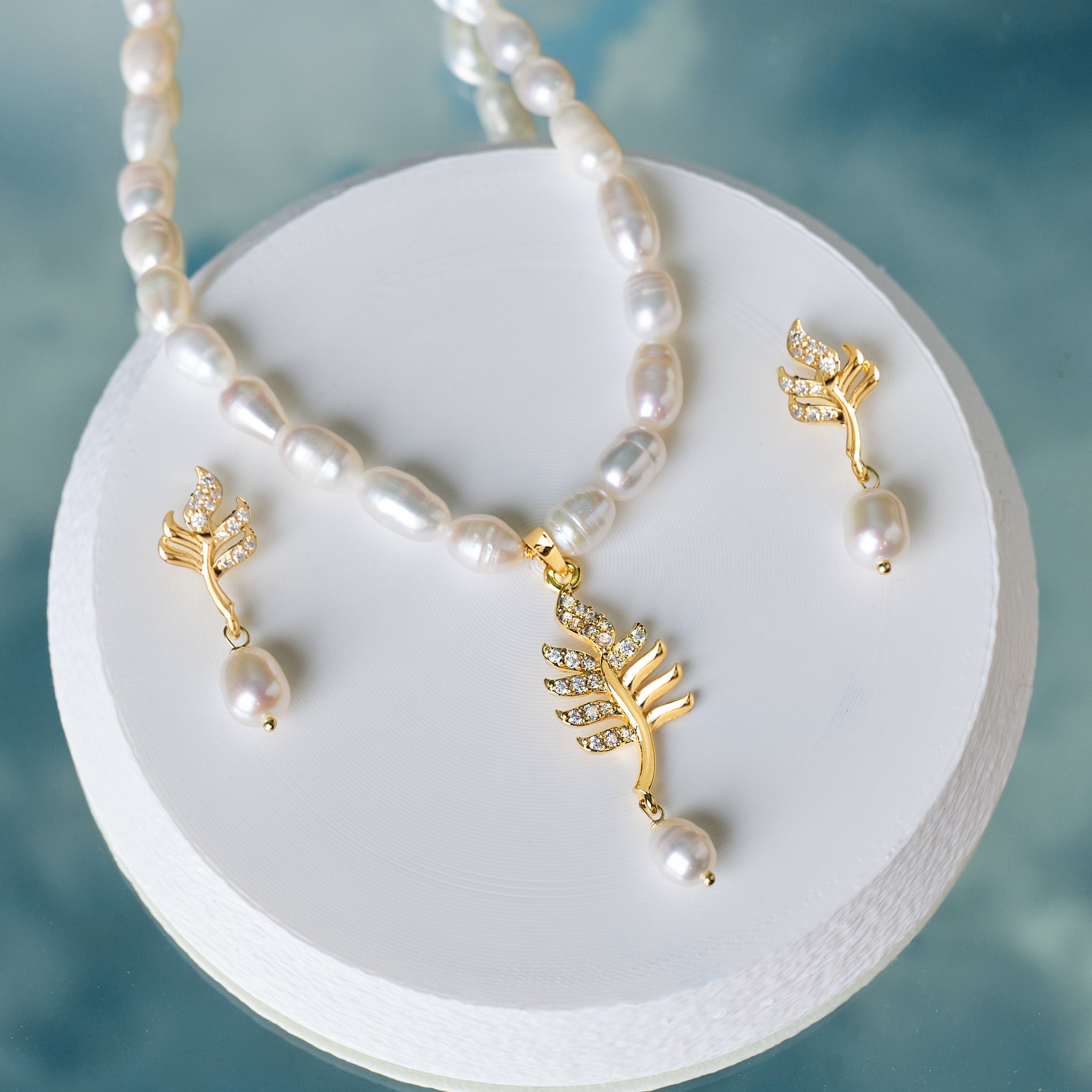 The Elegant Pearl & CZ Necklace Set by Chandrani Pearls features gold leaf designs with CZ crystals and pearls, elegantly displayed on a round white platform.