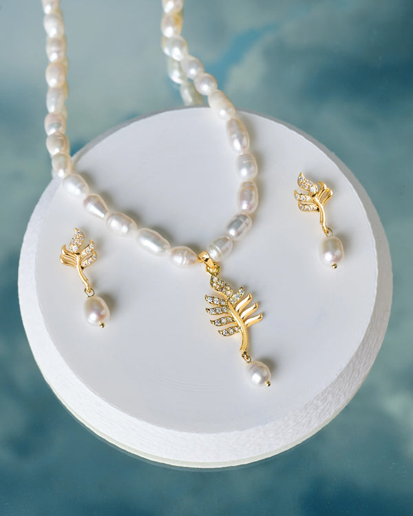 The Elegant Pearl & CZ Necklace Set by Chandrani Pearls features gold leaf designs with CZ crystals and pearls, elegantly displayed on a round white platform.