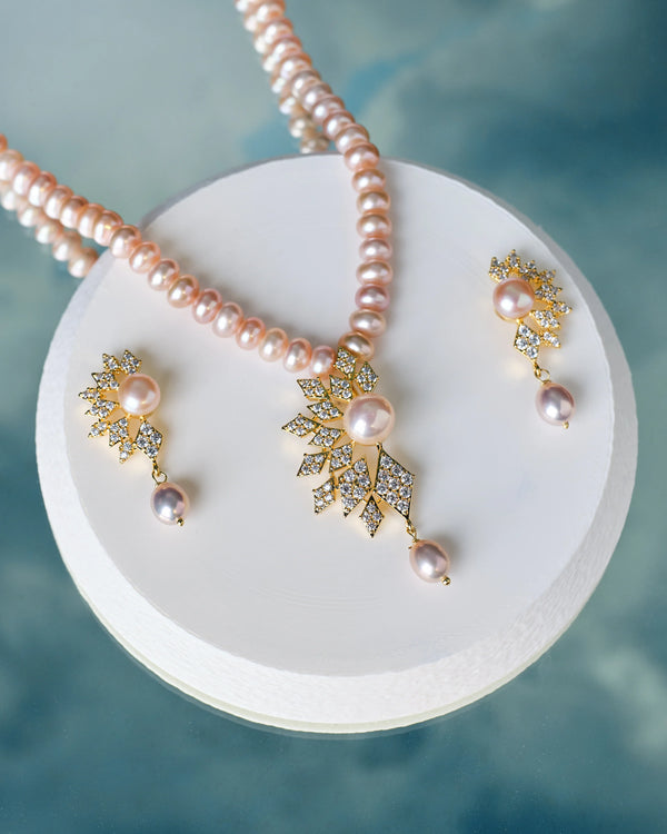 The Chandrani Pearls Layered Pearl & CZ Necklace Set, featuring pearls and CZ accents, is displayed on a white circular stand against a blue background.