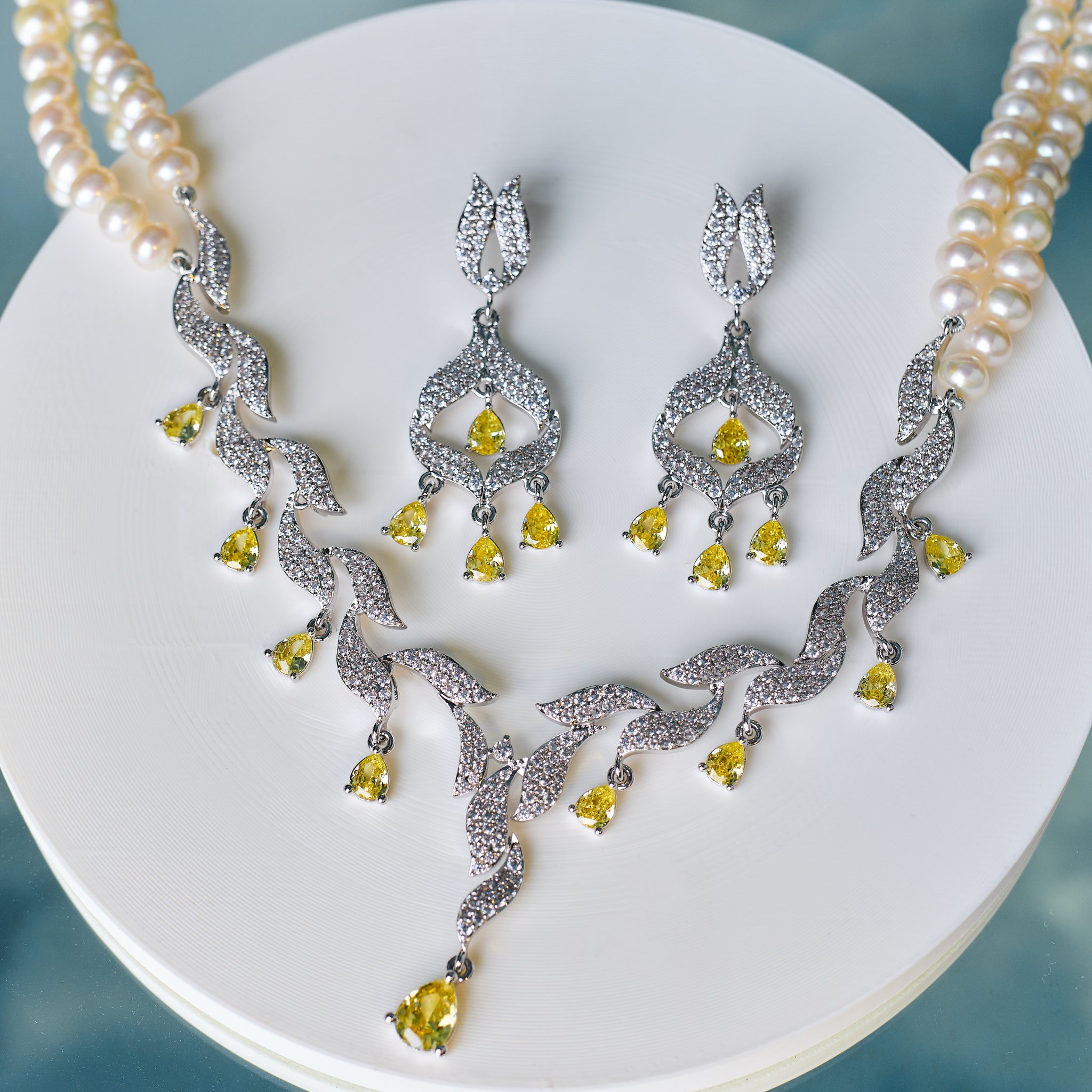 The Vintage-Inspired Bridal Pearl Set by Chandrani Pearls features a pearl necklace with a diamond and yellow gemstone pendant, CZ accents, and matching drop earrings—ideal for commemorating unforgettable moments.