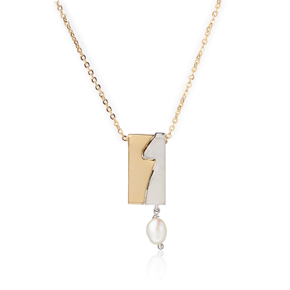 Wearing the Selene Pearl Pendant by Chandrani Pearls—a gold necklace with a rectangular wavy design and hanging pearl—paired with a white blazer, exudes timeless elegance.