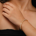 A close-up of a hand resting on a shoulder, adorned with the Chandrani Pearls Starry Night Bangle in 18K gold—a thin bracelet studded with delicate diamonds—radiating celestial elegance against a black background.