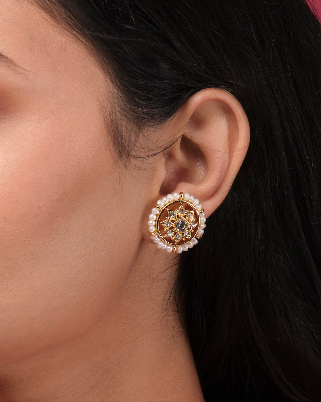 Traditional Beautiful CZ Earrings by Chandrani Pearls India, featuring round gold pearls with crystal accents, are elegantly displayed on a white stand against a blurred floral background.