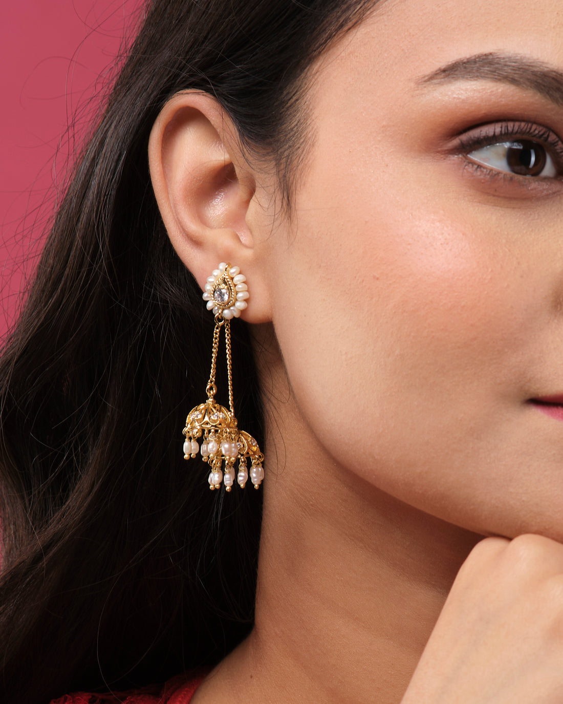 Beautiful Double Jhumka earrings by Chandrani Pearls India, with gold finish and pearl accents in a classic design, displayed on a white cube against a blurred floral background.