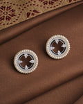 The Noor Moonlit Mirage Studs by Chandrani Pearls feature round pearls with a delicate silver border, elegantly displayed on brown fabric—perfect for any occasion.