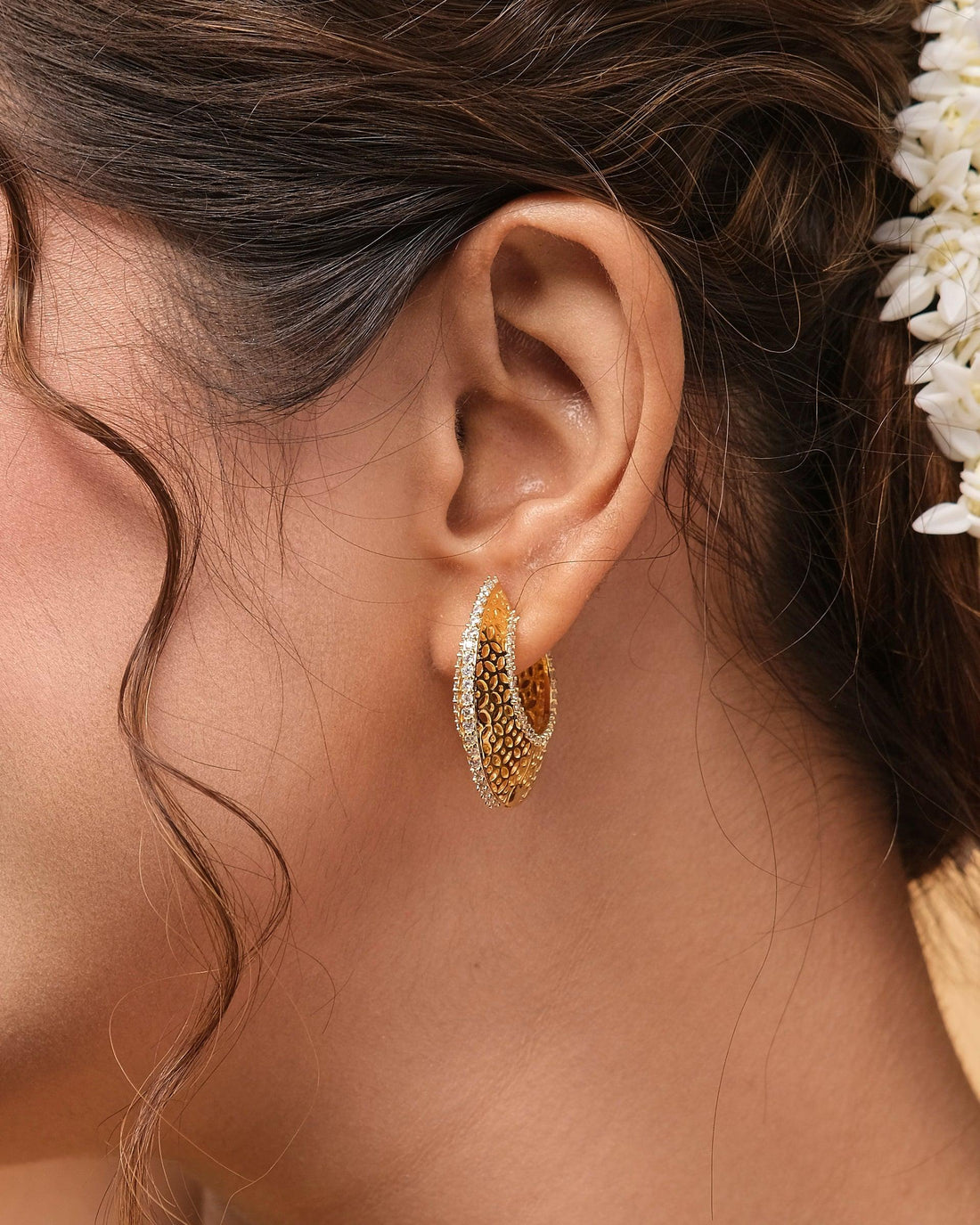 Two intricately designed Vivaciously Designed Huggie Silver Earrings from Chandrani Pearls in front of a red velvet box, placed on a dark blue surface.