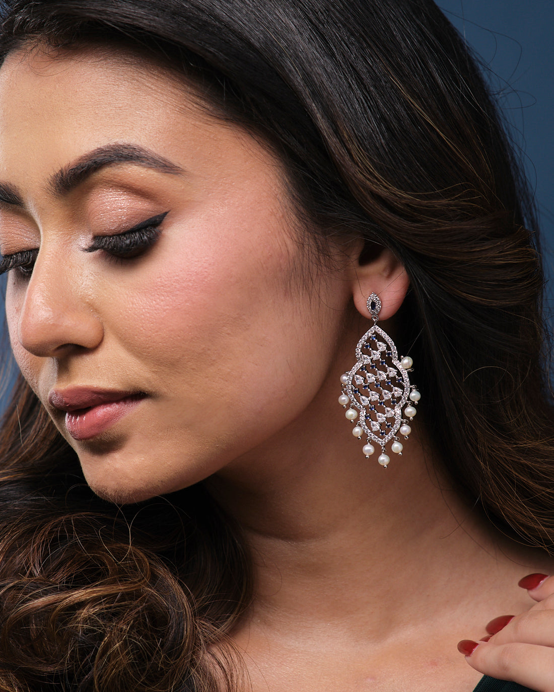 Navodha - The Wedded Dazzle Pearl Earrings by Chandrani Pearls, featuring diamond patterns and pearl accents, elegantly displayed on a textured green surface.