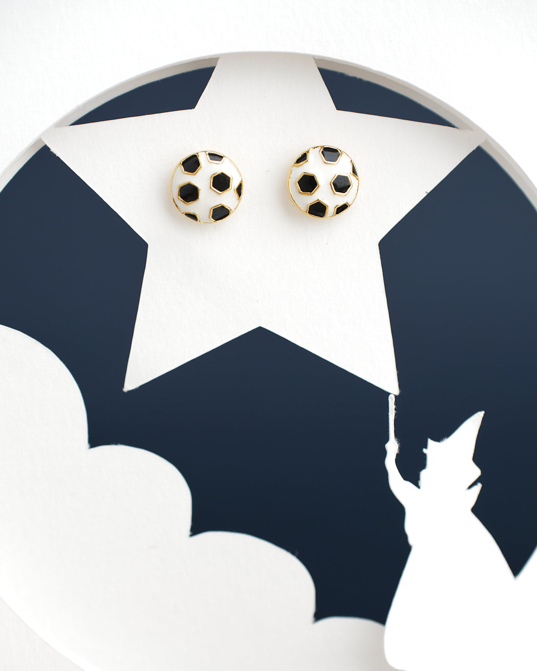 Football Style Stud Earrings from Chandrani Pearls India are showcased on a star cutout featuring a silhouette of a figure in a hat pointing a wand.