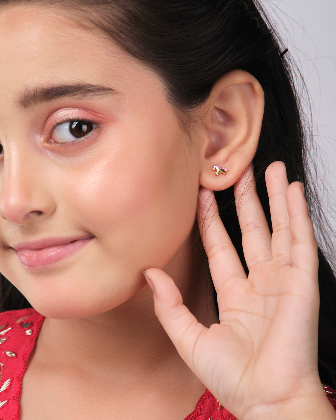A pair of The Cute Foal Stud Earrings by Chandrani Pearls India with pink manes sits on a white star cutout against a dark background, beneath which a wizard silhouette points a wand.