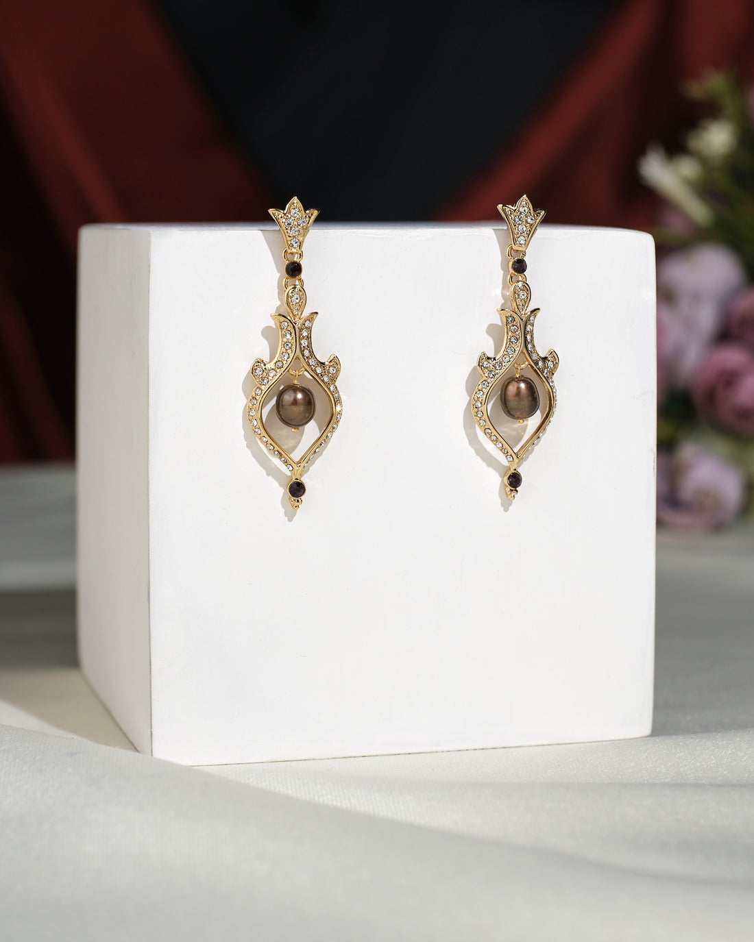 Elevate your style with Trendy Hang Earrings by Chandrani Pearls India—ornate gold dangle earrings adorned with elegant central pearls and small gemstones, beautifully presented on a white cube.