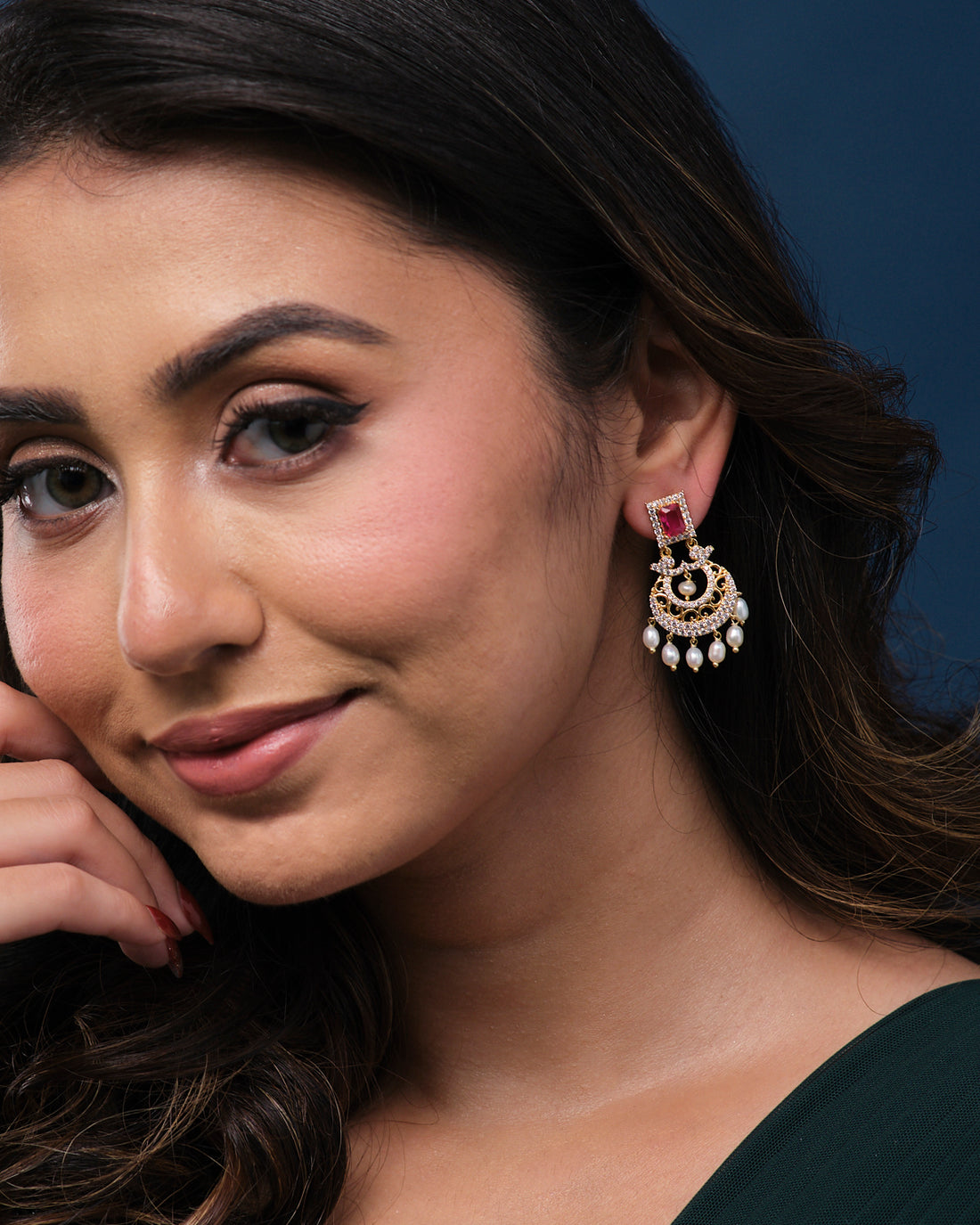 Gold ornate "Sparkling Wreath Pearl Earrings" by Chandrani Pearls, featuring red square stones and dangling pearls, are elegantly displayed on a green textured box.