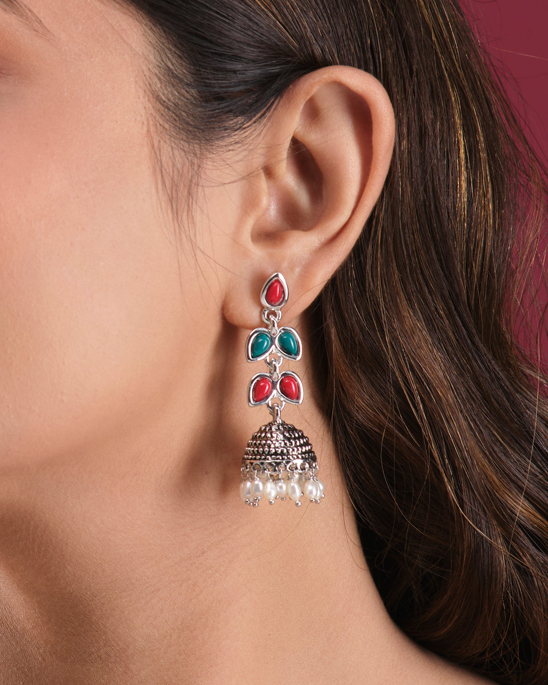 The Oxidised Pearl Jhumki by Chandrani Pearls India features silver elegance with red and green stones plus hanging white pearls, displayed on a white block—perfect for a radiant look and timeless style.