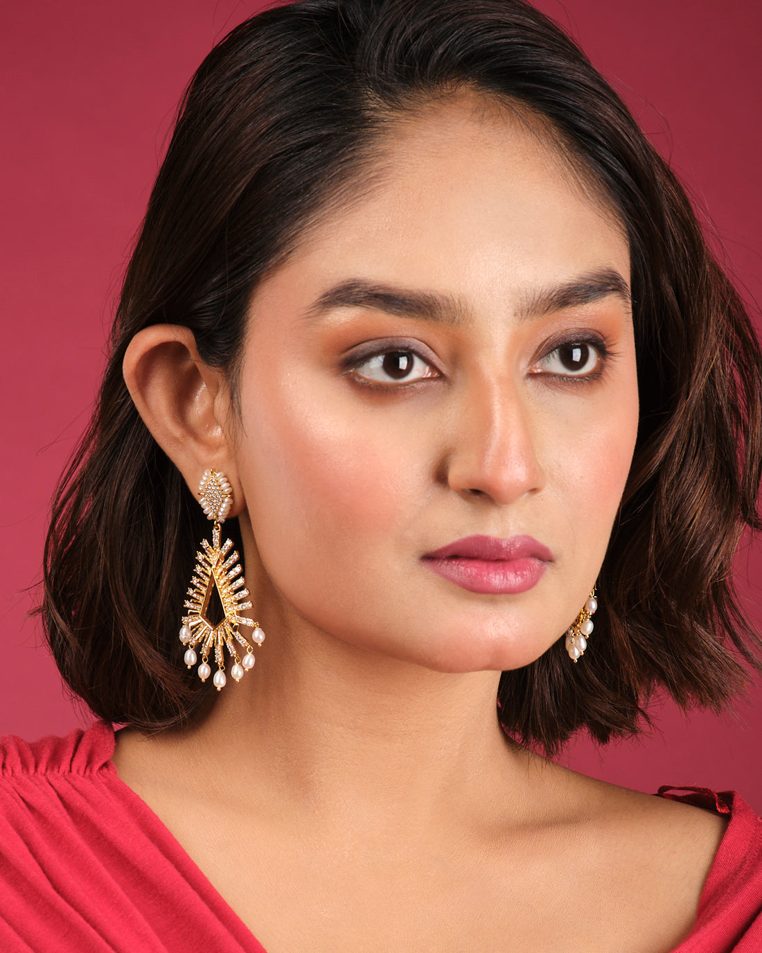 Define your Victory Hang Jhumki by Chandrani Pearls India: gold-toned geometric chandelier earrings with sparkling stones and pearl-like drops, elegantly displayed on a white cube—ideal for elevating any outfit.
