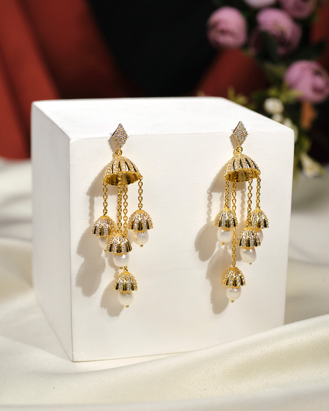 The Embellished Radiance Earrings by Chandrani Pearls India feature gold and pearl chandelier design with dome accents and dangling chains, adding luxury to any outfit. Displayed elegantly on a white box.