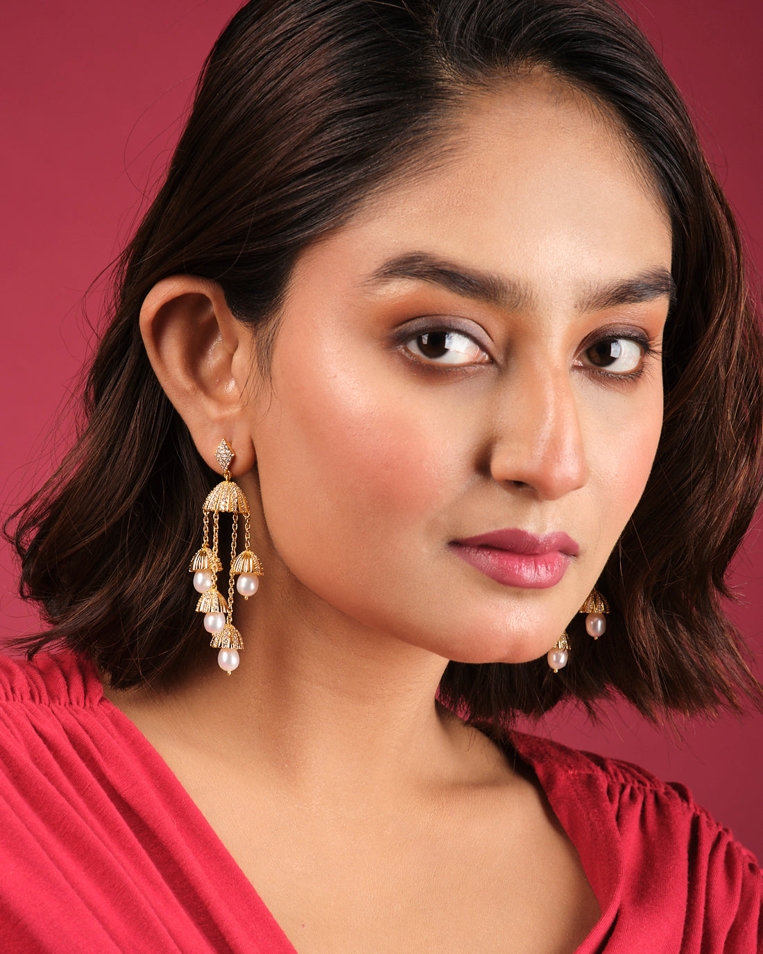 The Embellished Radiance Earrings by Chandrani Pearls India feature gold and pearl chandelier design with dome accents and dangling chains, adding luxury to any outfit. Displayed elegantly on a white box.
