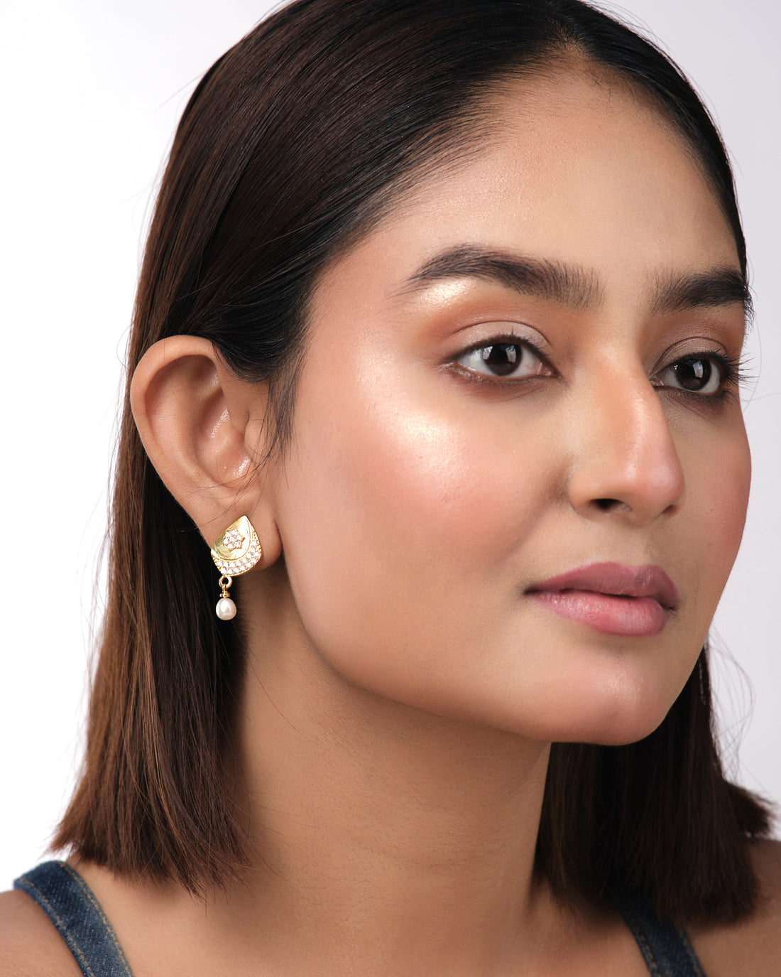 Fashionable Hanging Pearl Earrings by Chandrani Pearls India feature gold accents, small white crystals, and a radiant pearl on each earring, elegantly displayed against a pale yellow background.