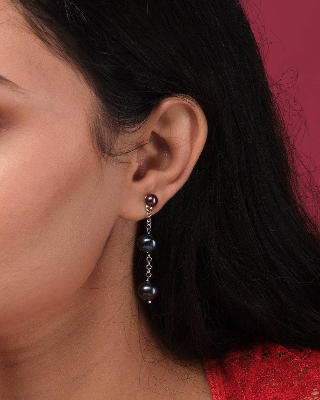 Chandrani Pearls India's Stylish Hang Pearl Earrings feature three black pearls on each earring, linked by silver chains. Displayed on a white block with a blurred floral background, they offer timeless elegance.