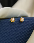 Delicate pearls suspended beneath radiant CZ studs by Chandrani Pearls are elegant gold earrings featuring central pearls and sparkling CZ accents, presented on a textured blue surface for a sophisticated look.