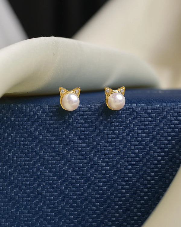 These stud earrings from Chandrani Pearls feature a flawless pearl and exude grace and glamour, resting elegantly on a textured dark blue surface with a white fabric backdrop.