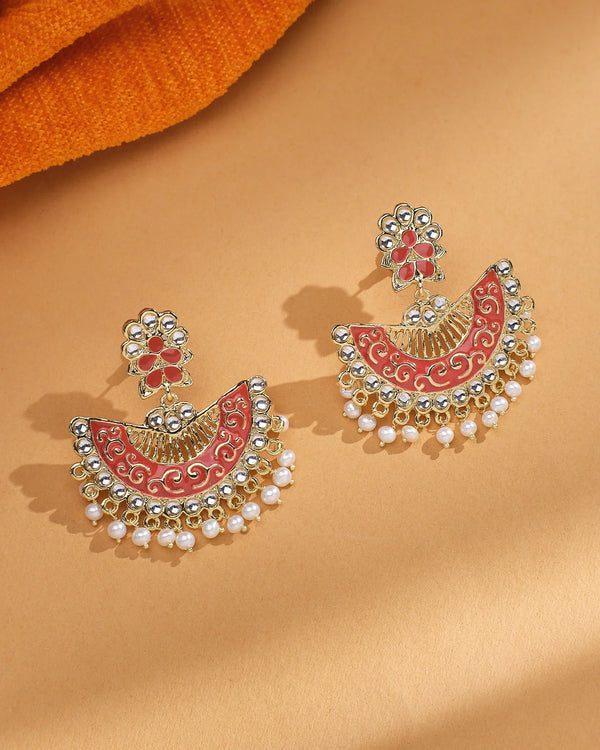 The Chandrani Pearls Festive Shine Enamel Pearl Jhumka features gold-toned and red enamel floral designs with CZ accents and dangling white pearls, presented on a beige surface.