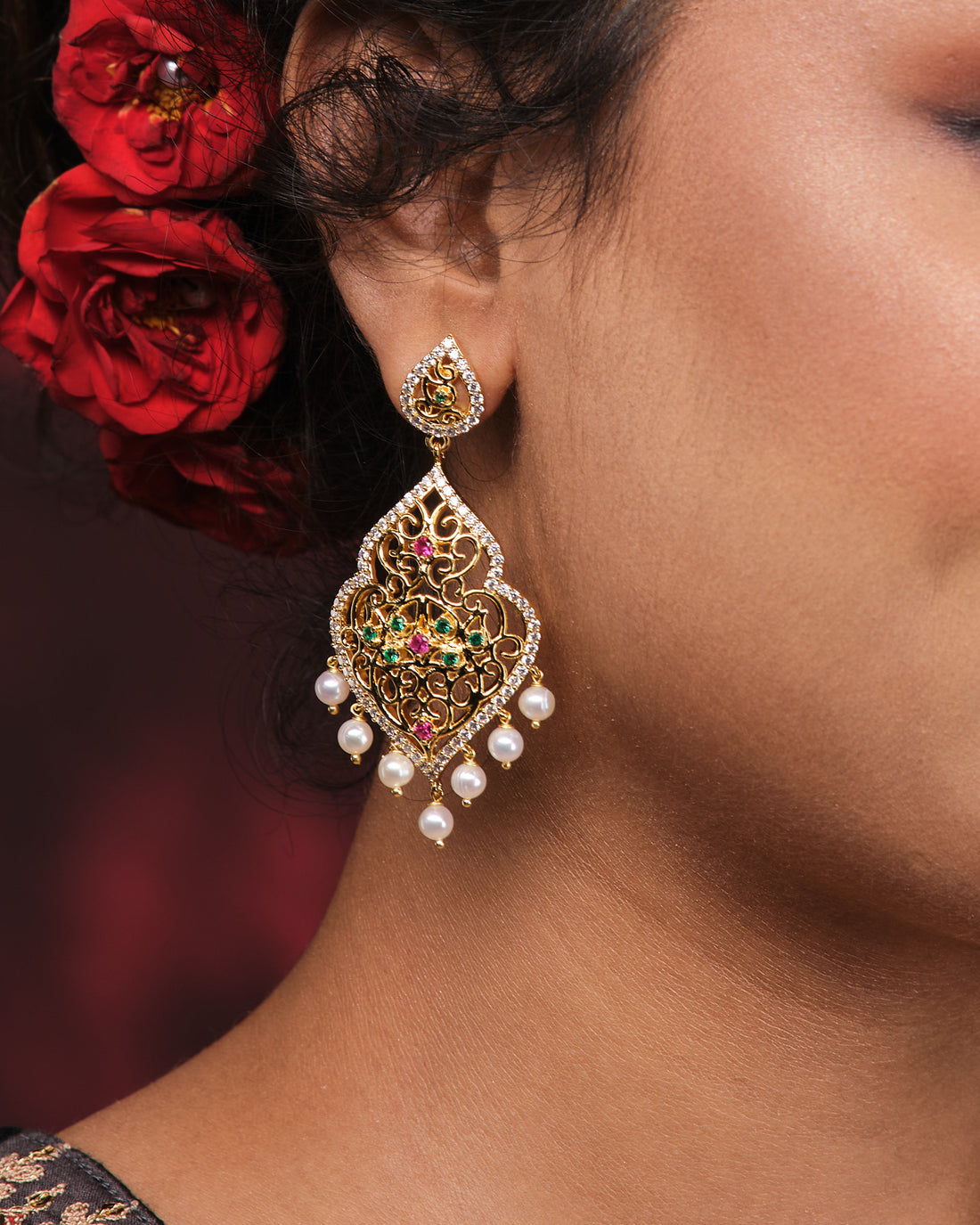 The Zuly Multi Stone Pearl Earrings by Chandrani Pearls feature ornate gold, colored enamel, and iridescent pearl dangles—ideal statement cocktail earrings—shown against a black box with red fabric accents.