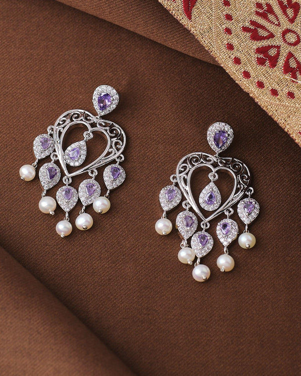 The Chandrani Pearls Elegant Pearl Jhumka Earrings in Rodium Finish Design, adorned with purple gemstones and white pearls, add a touch of sophisticated charm to your ethnic look.