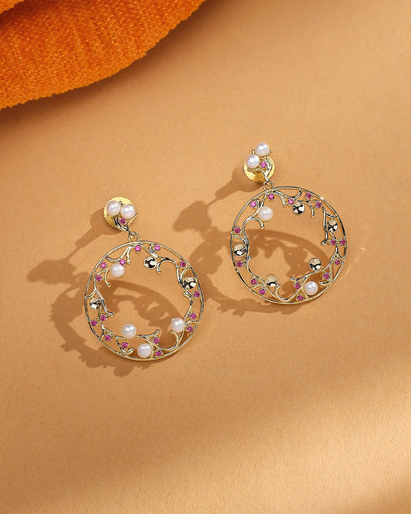 Golden Glam Pearl Earrings by Chandrani Pearls, featuring pearls, pink stones, and delicate CZ accents, displayed on a beige surface with orange fabric partially visible.