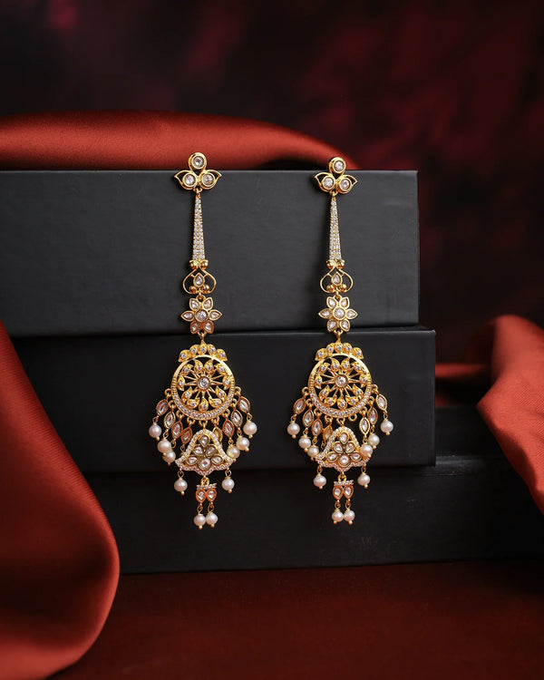 Dreamy Desire Pearl Earrings by Chandrani Pearls, featuring ornate gold and pearls with handcrafted twisted chains, are displayed on black boxes against a dark red satin background.