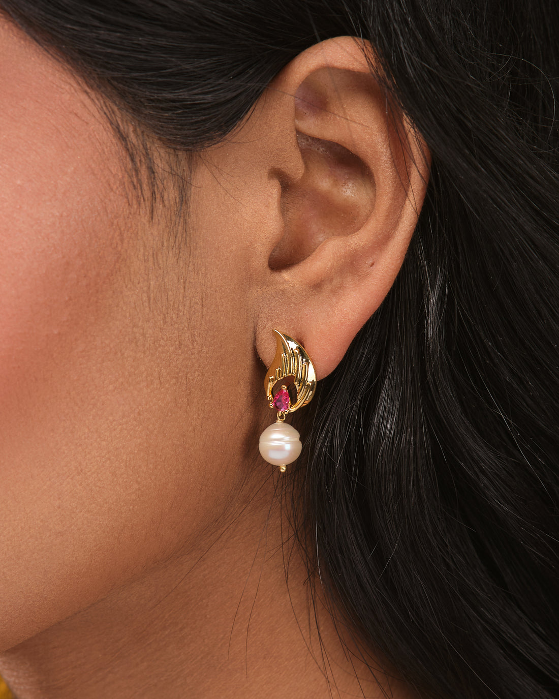 The Twilight Glow CZ Earrings by Chandrani Pearls feature gold with pearl highlights and red gemstone accents, displayed on beige with orange textured fabric—an elegant, twilight-inspired design for special evenings.