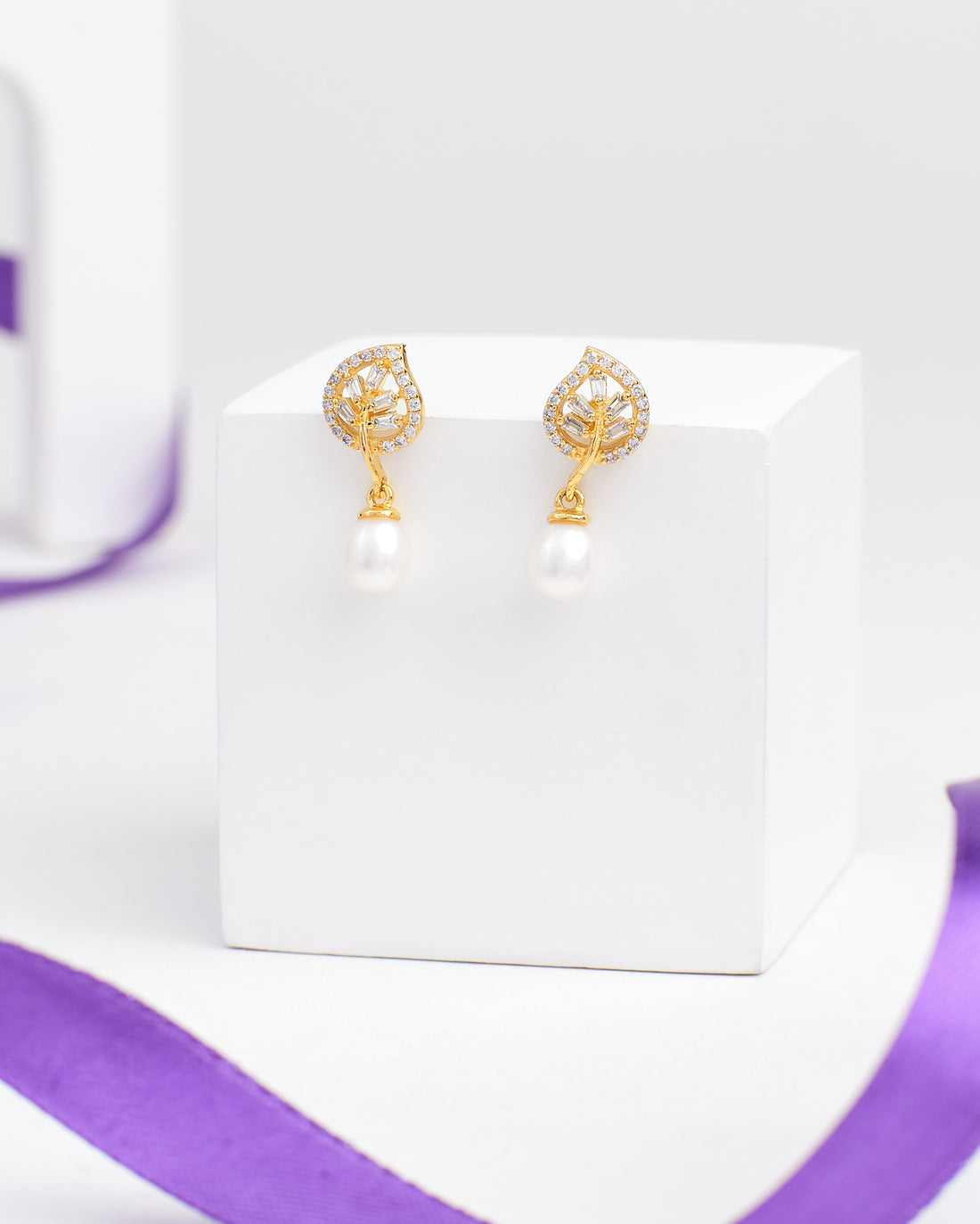 Sparkling Duo Silver Earrings by Chandrani Pearls feature a leaf-shaped design with clear stones and dangling pearls, radiating moonlight charm—an exquisite choice for lovers of delicate jewelry. Displayed on a white cube with a purple ribbon nearby.