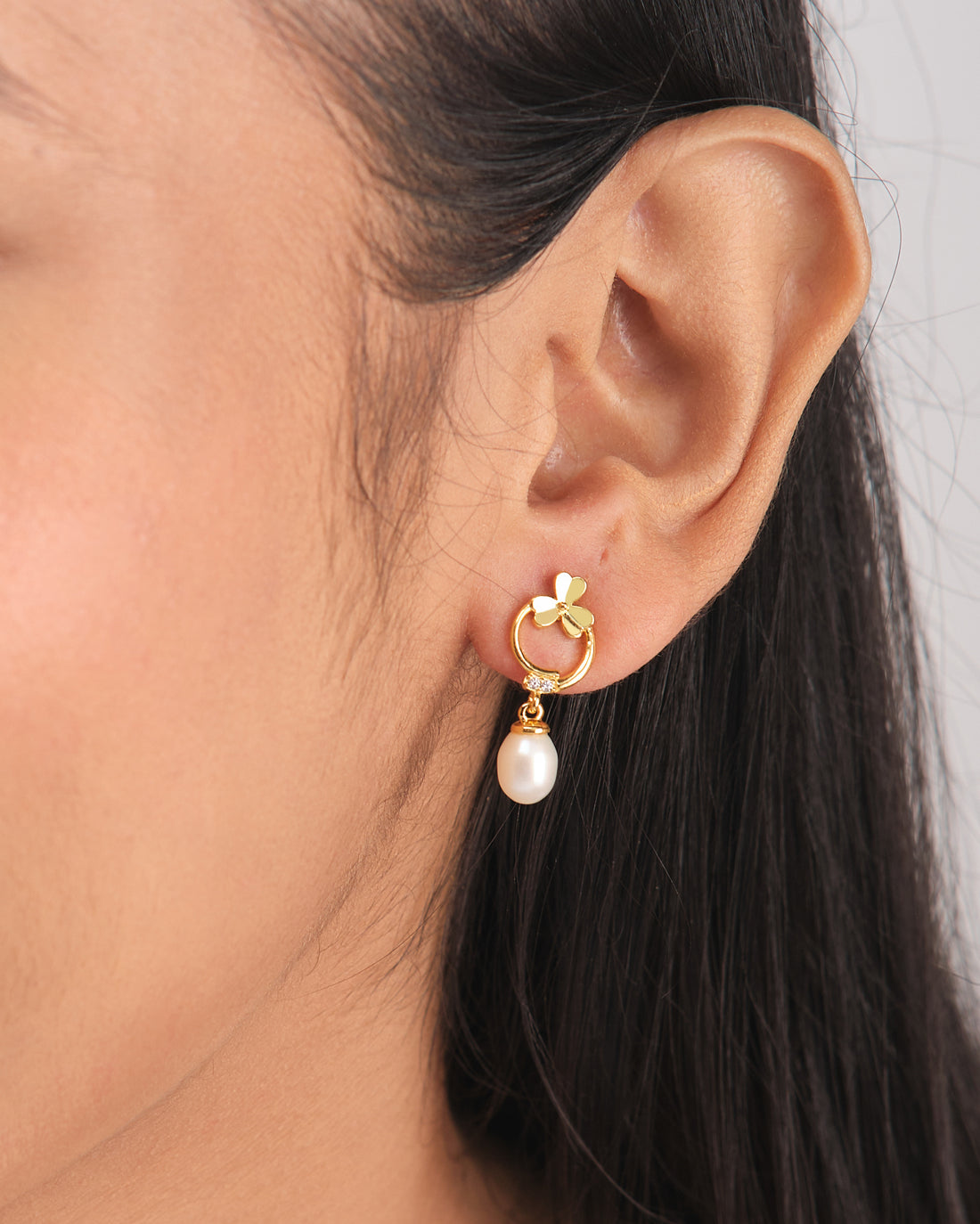 The Artsy Embrace Silver Earring by Chandrani Pearls features chic hoops with delicate bows and dangling white pearls, displayed on a white cube—perfect for elevating your style and embracing the demifine earring trend.