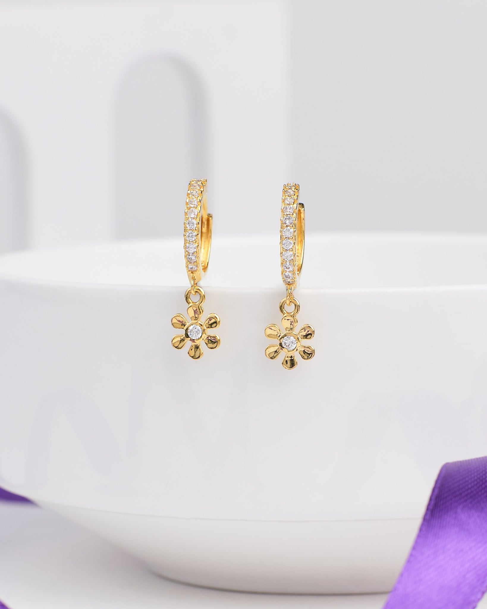 Glow Mood Silver Earrings by Chandrani Pearls feature flower-shaped pendants with stone-accented petals, adding a mood-lifting touch to your laid-back style and elegantly displayed over the rim of a white bowl.