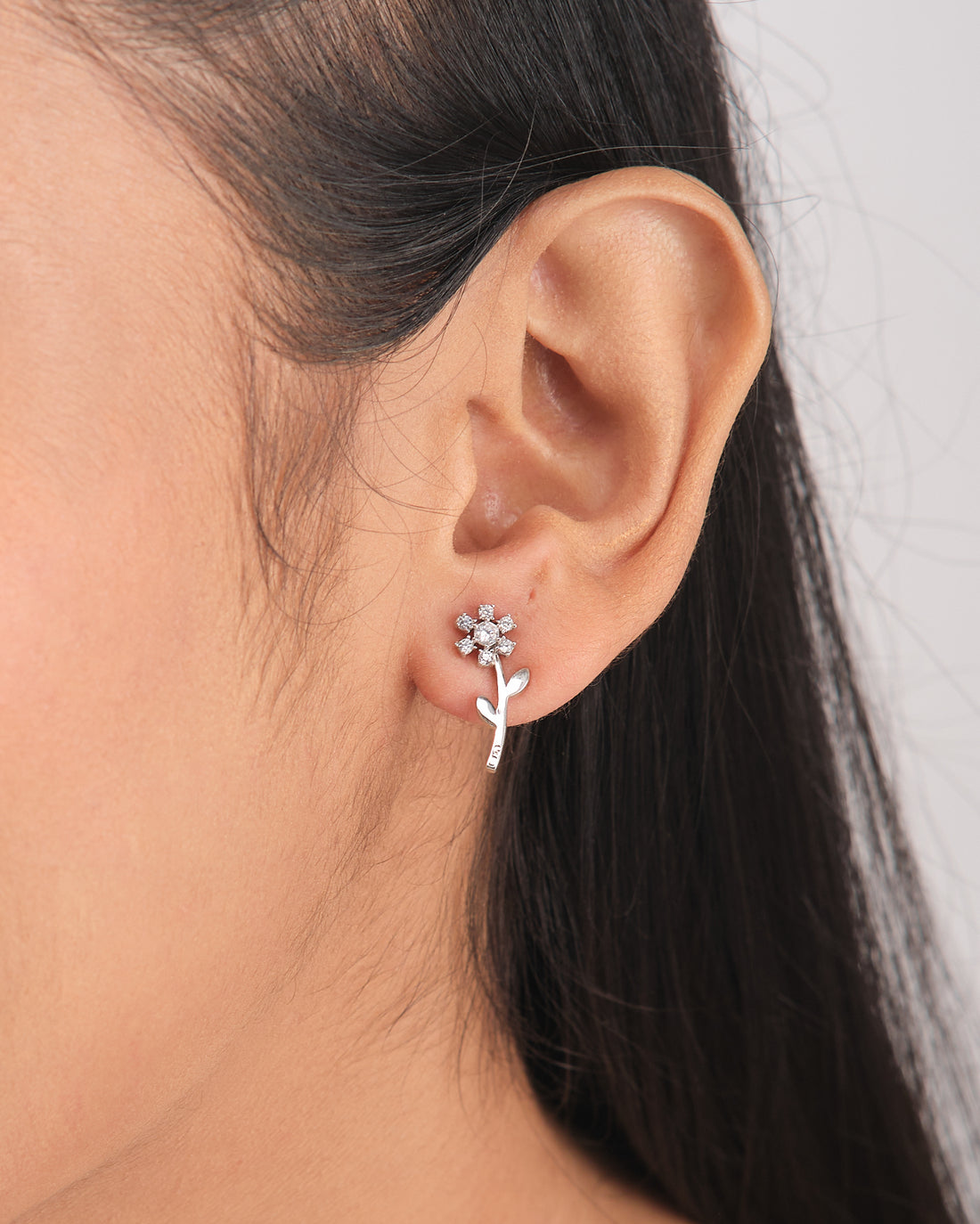 Glimmer Days Silver Studs by Chandrani Pearls—flower-shaped silver earrings with stems and leaves, ideal for daily wear—are shown resting on a white bowl, accented by a nearby purple ribbon.