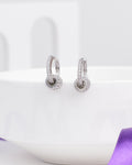 The Delicate CZ Hoop Earrings in Demifine Silver by Chandrani Pearls are lightweight, modern earrings with sparkling crystals—displayed on a white ceramic bowl and accented by a purple ribbon—ideal for any occasion.
