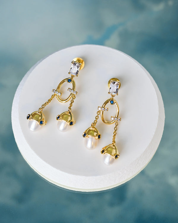 Chandrani Pearls' Stylish Handcrafted Pearl Earrings with CZ Sparkle are displayed on a round white platform against a blue background—perfect for adding everyday elegance.