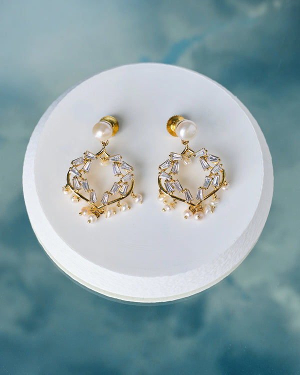 The Trendy Pearl & CZ Handcrafted Earrings by Chandrani Pearls feature gold hoops with pearl studs and geometric accents, displayed on a round white platform set against a blue background.