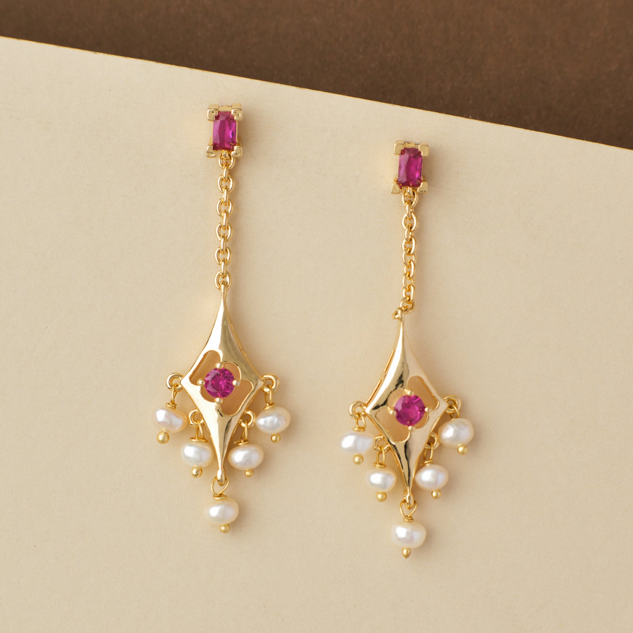 Ethnic Pearl Hanging Jhumkas with pink gemstones and pearl accents on a beige background by Chandrani Pearls India.